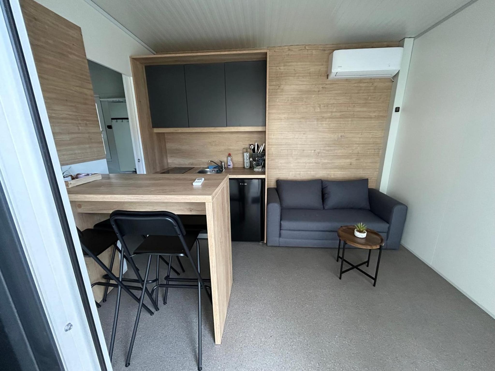 Kuhinjski kotiček z jedilno mizo in sivim kavčem v 24 m² veliki tiny hiški